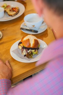 A burger on a pretzel bun next to a cup at the restaurant table, autumn creations, Cafe Kuh,