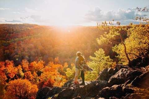 A couple embraces on a rocky overlook, surrounded by vibrant autumn foliage in Quebec, Canada. The