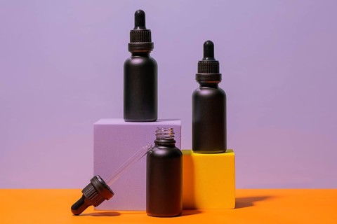 Elegant black dropper bottles are displayed against a vibrant purple and orange background. The