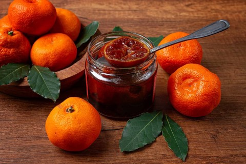 Jar of tangerine jam, stands on a wooden table, with fresh tangerines