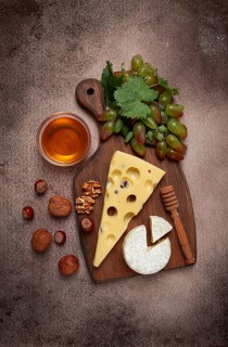 Cheese with big holes, emmental, maasdam, brie cheese, on a cutting board, with grapes and honey,