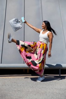 A woman in a vibrant, colorful outfit strikes a joyful pose in front of modern architecture,