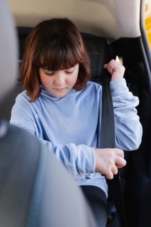 A child in a light blue hoodie fastens the seatbelt in the backseat of an electric car. Focus on