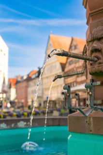 Close-up of flowing water from a fountain spout with historic buildings, Nagold, Black Forest,