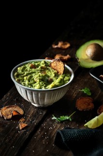 Top view of bowl of fresh guacamole placed near avocado and chips on weathered lumber tabletop