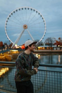 Side view of man in a colorful sweater leans on a railing, smiling as the iconic Montreal Ferris