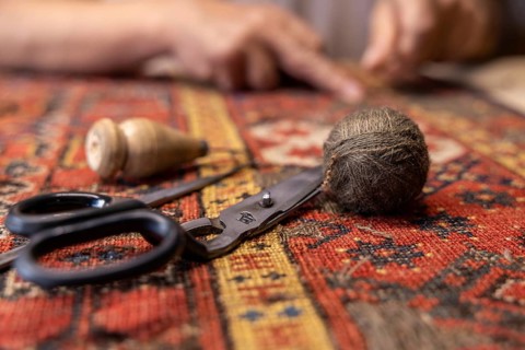 Cropped unrecognizable senior male Iranian carpet restorer meticulously works on repairing a