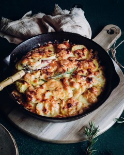 A delicious potato gratin with melted cheese and fresh rosemary in a cast iron skillet. Presented