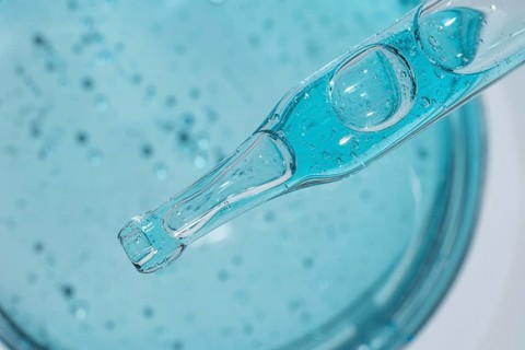Close-up of blue cosmetic gel with visible droplets and texture, captured from above. A clear
