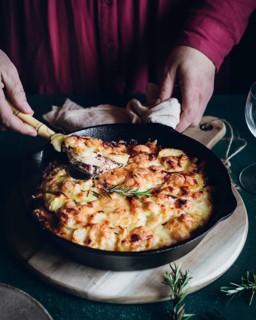 A homemade potato gratin casserole baked to golden perfection in a cast iron skillet. A person