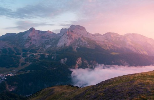 A stunning mountain landscape captured during dawn, with warm pink hues illuminating the rocky
