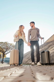 A young couple walks hand in hand with suitcases, exploring Majorca, Spain. They're on a sunny