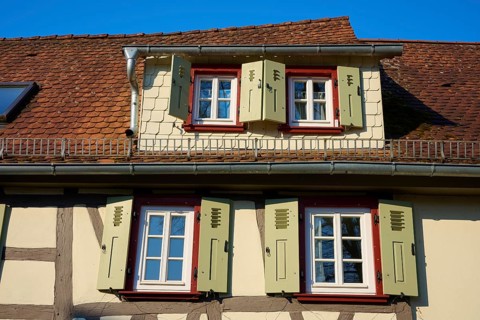 A traditional half-timbered house roof with projecting shutters and blue sky in the background,