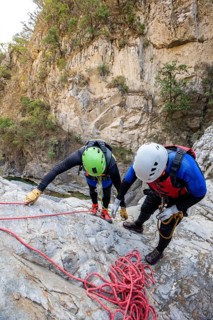 Two canyoneers equipped with safety gear meticulously prepare for a thrilling descent in the rugged