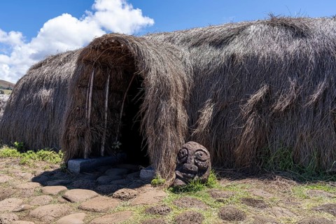 Traditional grass house (Hare Paenga) with entrance and small stone sculpture in front,