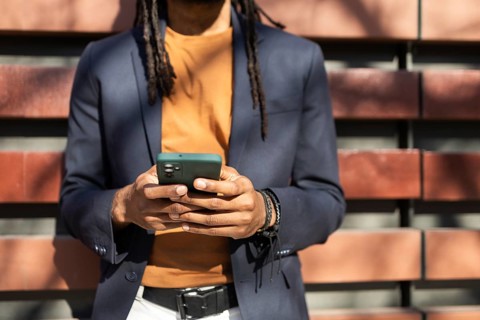A cuban business man dressed in a blue blazer and orange shirt uses a smartphone while standing