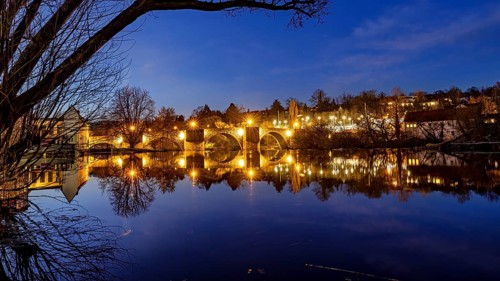 Evening scene with illuminated bridge and reflecting river at night, The historic Bartenwetz stone