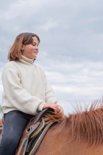 A young girl wearing a cozy sweater enjoys a peaceful ride on a horse at a farm, surrounded by a