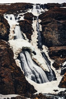 A powerful vertical shot of Rjukandi Waterfall flowing down a rugged, snow-patched cliff in eastern
