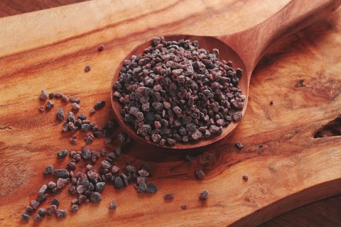Crystals of black salt, on a wooden spoon, laid out on a wooden surface, top view