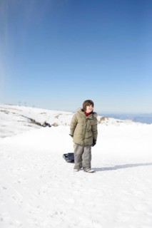 A child in a winter coat stands on a snowy landscape at Sierra Nevada Ski Resort, Granada. Clear
