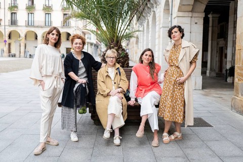 A group of five stylish women pose confidently on a city street. They exhibit unique fashion