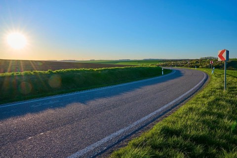 Street at sunset, which runs through soft, green landscape, bright sky and peaceful atmosphere,