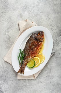 Baked dorado fish, in the oven, fried dorado, with spices and herbs, on a white plate, top view,