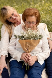 A serene moment capturing an elderly woman holding a bouquet while being lovingly embraced by her