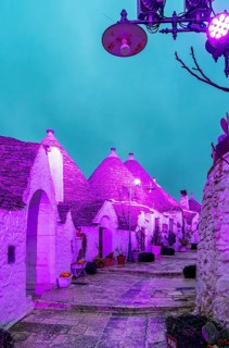 Trulli houses illuminated in purple light, Rione Monti, Alberobello, Apulia - Puglia, Italy