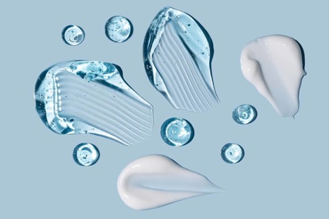Various clear gel and white cream textures smeared and dotted on a pastel blue surface, showcasing