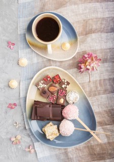 A pieces of homemade chocolate with coconut candies and a cup of coffee on a gray concrete