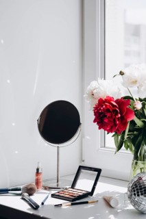 A modern home setting features vibrant red and white peonies in a vase by a window, alongside a