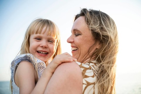 A cheerful mother and daughter share a joyful moment on a sunlit beach in Italy. The warmth of