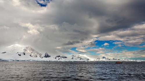 Snowy mountain landscape by the sea under a dramatic sky with dark clouds and a small boat, The