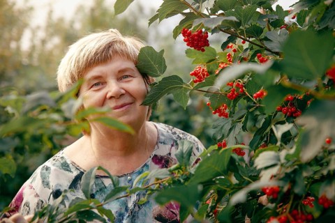 An elderly woman stands amid lush foliage and bright red berries in a vibrant garden in Khakassia,