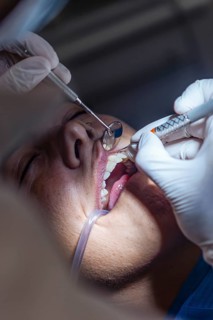 A dentist wearing gloves performs a teeth cleaning using a syringe and tools in a patient mouth.