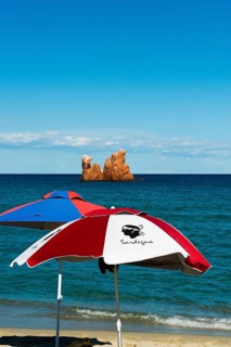 Sunshades on the beach and red rocks, Spiaggia di Cea, Tortoli, Sardinia, Italy