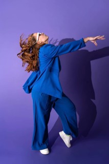 A young woman dancer in a vibrant blue outfit gracefully performs against a striking purple