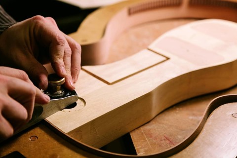 Hands meticulously crafting a bass guitar body in a luthier‚Äôs workshop. The image captures the
