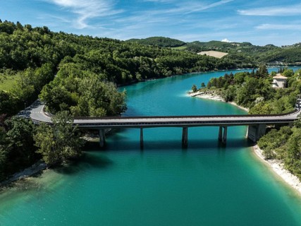 Aerial view of a bridge spanning the vibrant turquoise waters of Lago di Fiastra, surrounded by