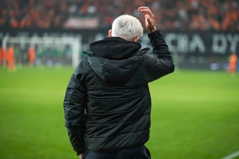 Head coach's back and soccer match at the stadium in the background.