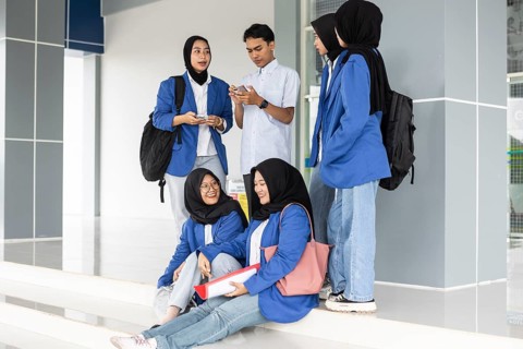 A group of Asian Muslim students gather at the school entrance, dressed in uniforms and carrying