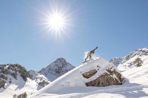 A snowboarder carves through untouched powder in a breathtaking backcountry mountain landscape. The
