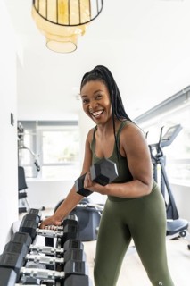Smiling businesswoman picks up a dumbbell while exercising in a hotel gym during her business trip,