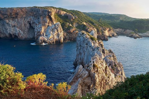 Steep cliffs and rocky coast stretch under cloudy sky on the coast, morning light, islet of Tsichli