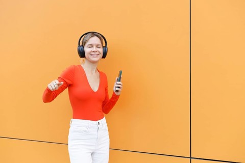Woman in Warsaw enjoying music with headphones and smartphone She stands against a vibrant orange