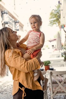 A mother lovingly holds her young daughter in an outdoor setting. The sun is shining, creating a
