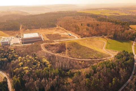 Wide view of a hilly area with industrial buildings, surrounded by forest and fields, old deposit