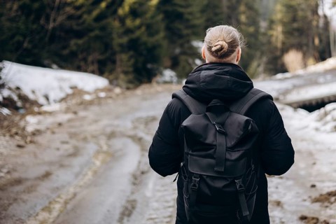 A young man with a backpack explores a snowy mountain forest. Dressed in warm clothing, he enjoys a